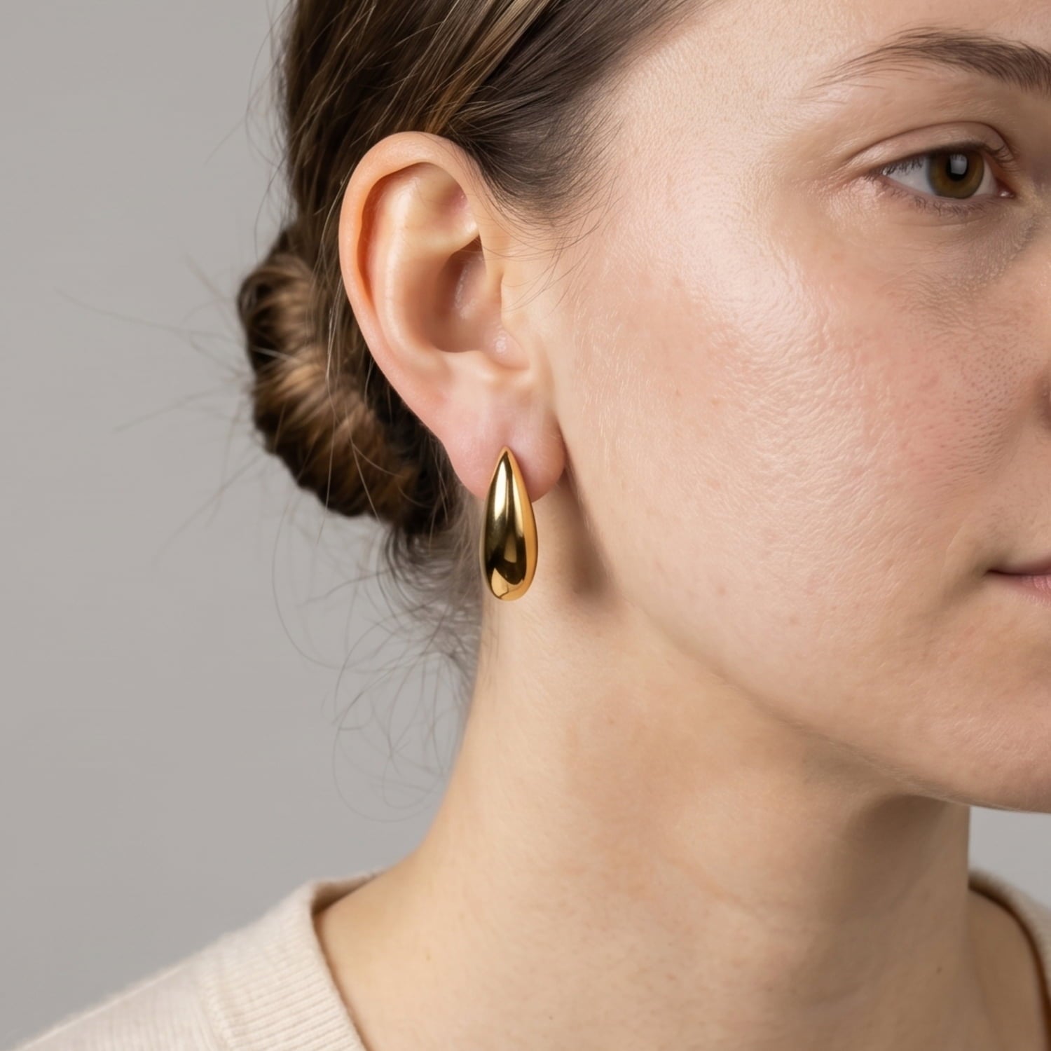 Close-up of an ear adorned with a single large gold vermeil earring featuring a smooth, elongated curved design, highlighting elegant contemporary silver jewellery by Azendi.
