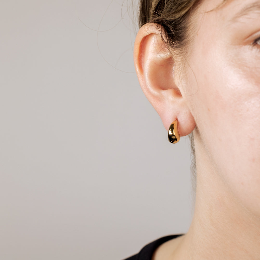 Close-up of an ear wearing a small, curved gold vermeil earring with a smooth, sculptural design, highlighting contemporary sterling silver jewellery craftsmanship.
