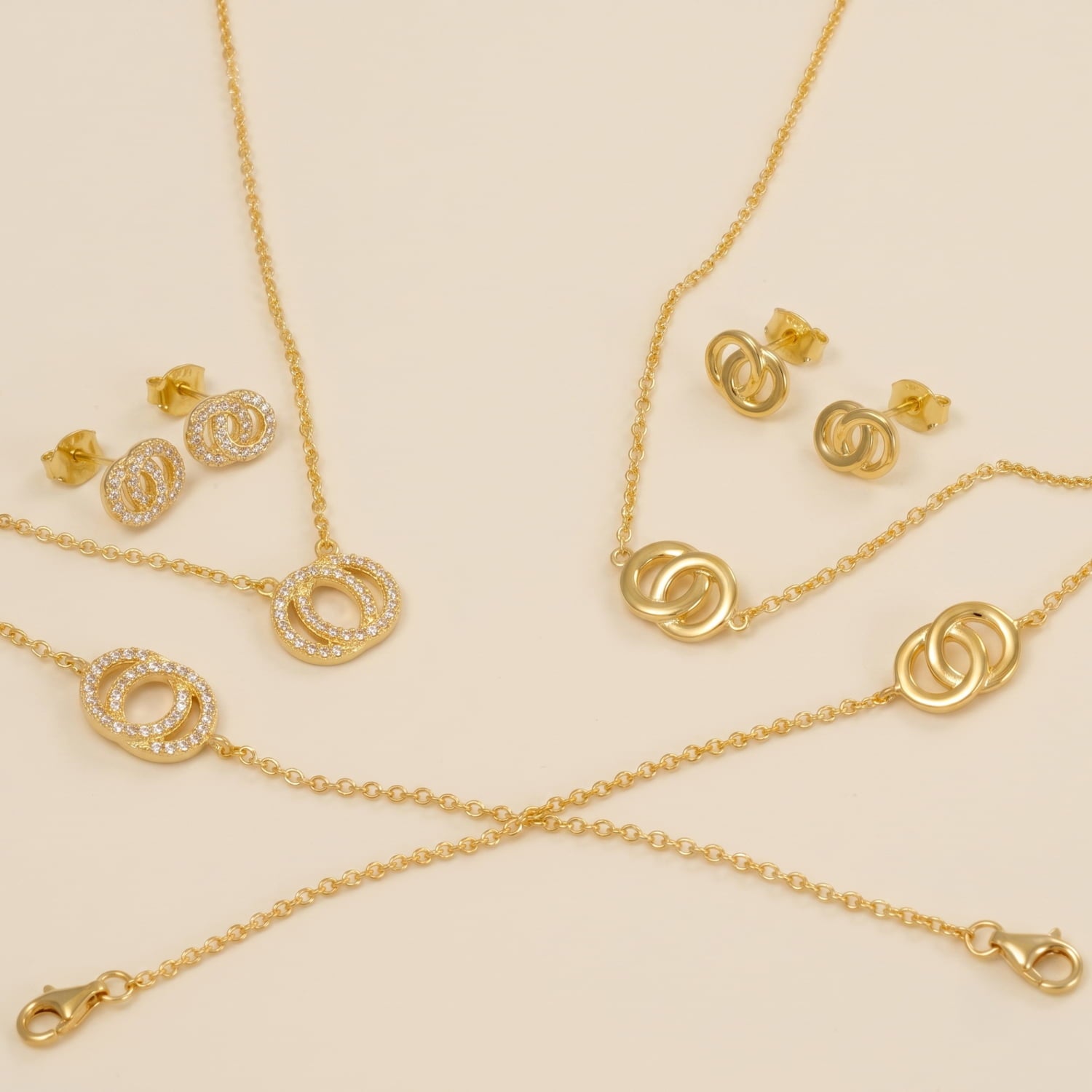 A collection of yellow gold vermeil jewellery featuring a sculptural interlocking design, with delicate chains on a soft fabric backdrop.