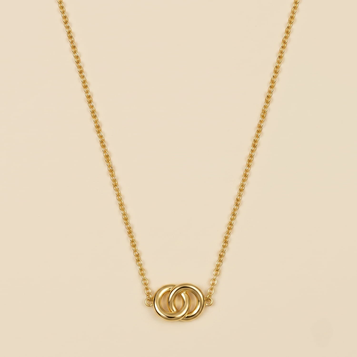 Yellow gold vermeil necklace featuring two interlocking circles on an adjustable chain, presented on a soft cream fabric background.