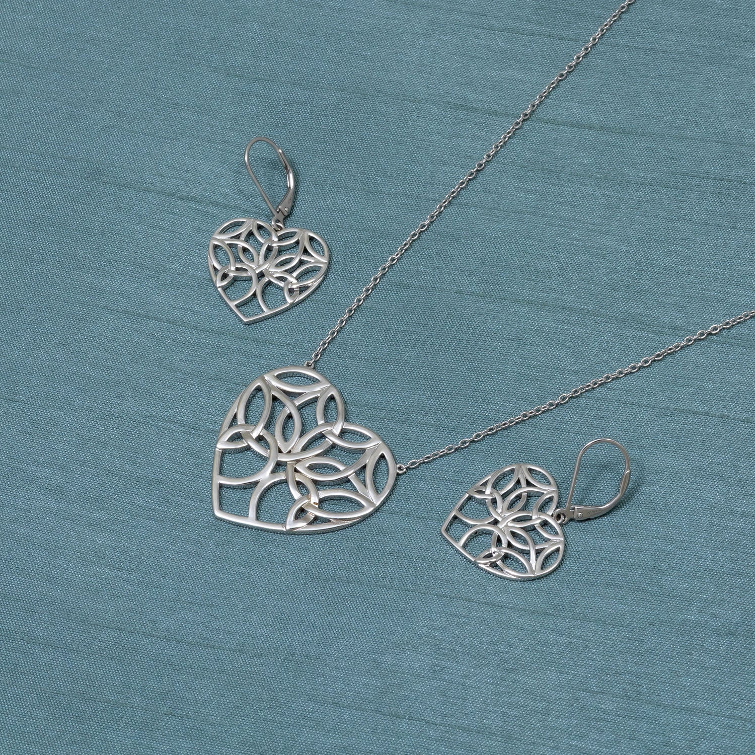 Sterling silver drop earrings featuring intricate Celtic Tree of Life heart motifs with openwork design, paired with a matching pendant necklace, showcasing sculptural elegance.