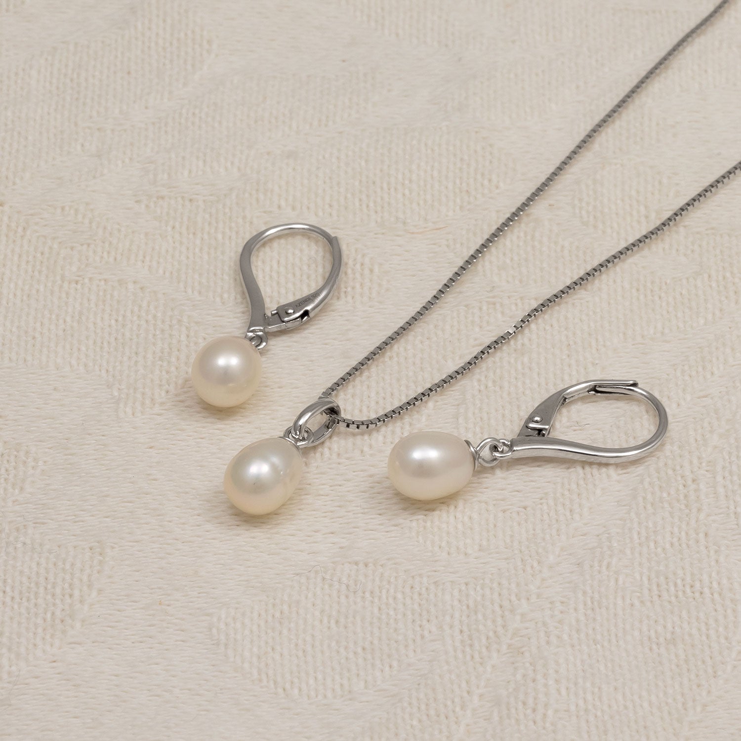 Pair of sterling silver drop earrings each showcasing a smooth teardrop freshwater pearl suspended from a secure hinged hoop, styled on a neutral textured background.