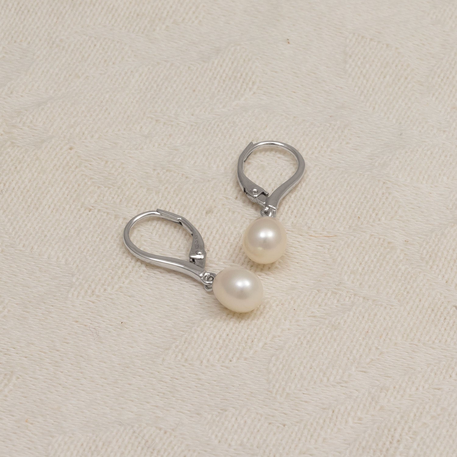 Pair of sterling silver drop earrings featuring 0.8 cm teardrop-shaped freshwater pearls suspended from secure lever-back clasps, displayed on a soft cream fabric background.