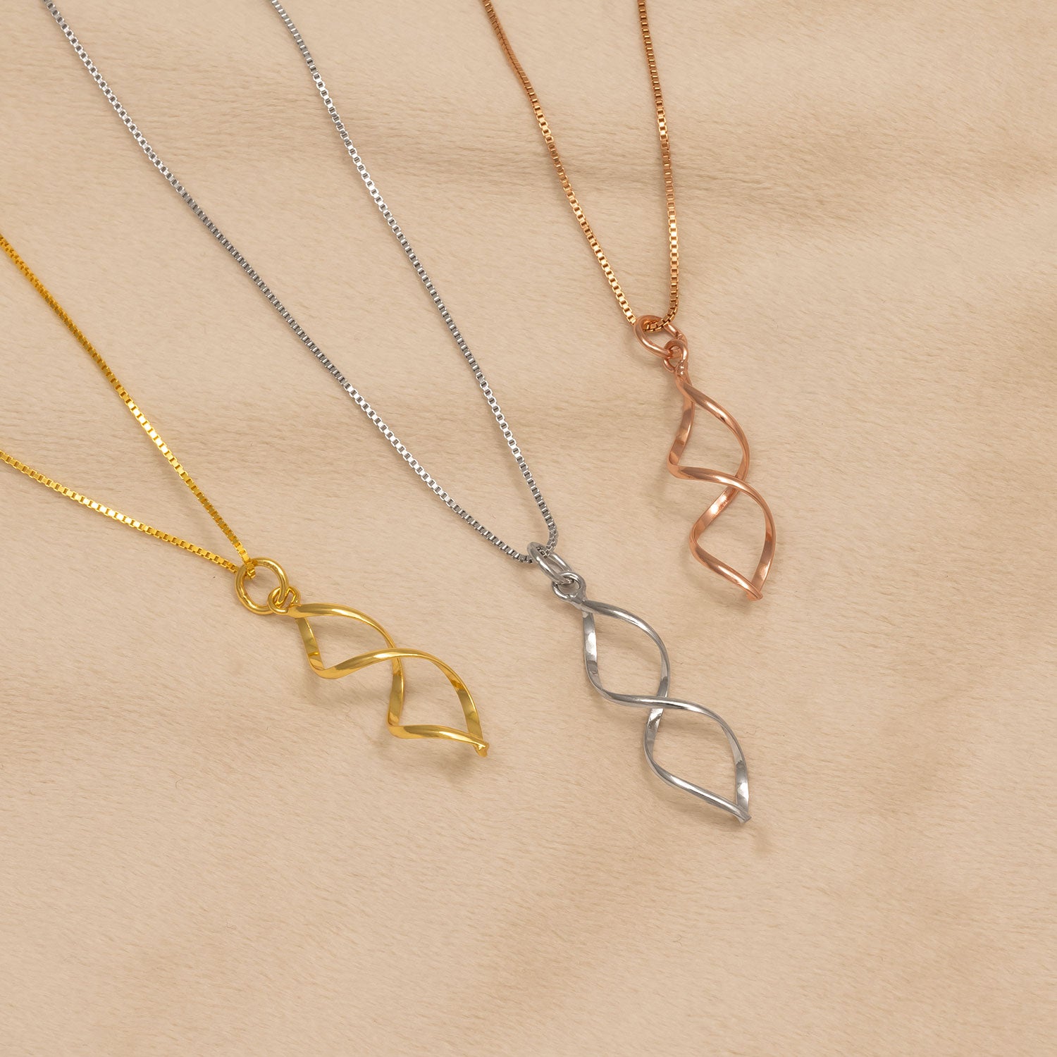 Three pendant necklaces featuring elongated open twisted designs in yellow gold vermeil, sterling silver, and rose gold vermeil, each suspended from delicate chains.