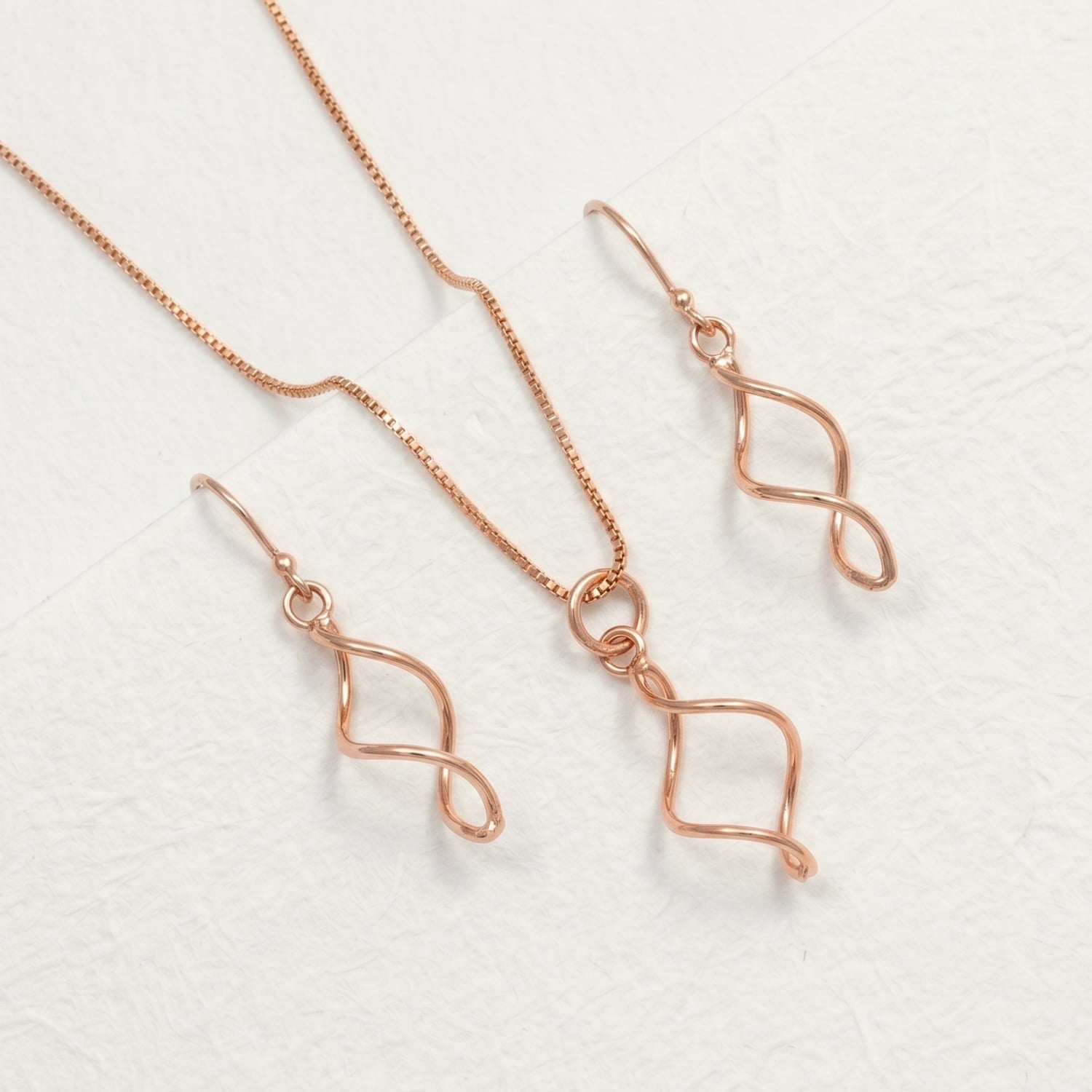 Delicate rose gold vermeil pendant necklace and matching earrings featuring a graceful twisted loop design, crafted with a modern, sculptural aesthetic.
