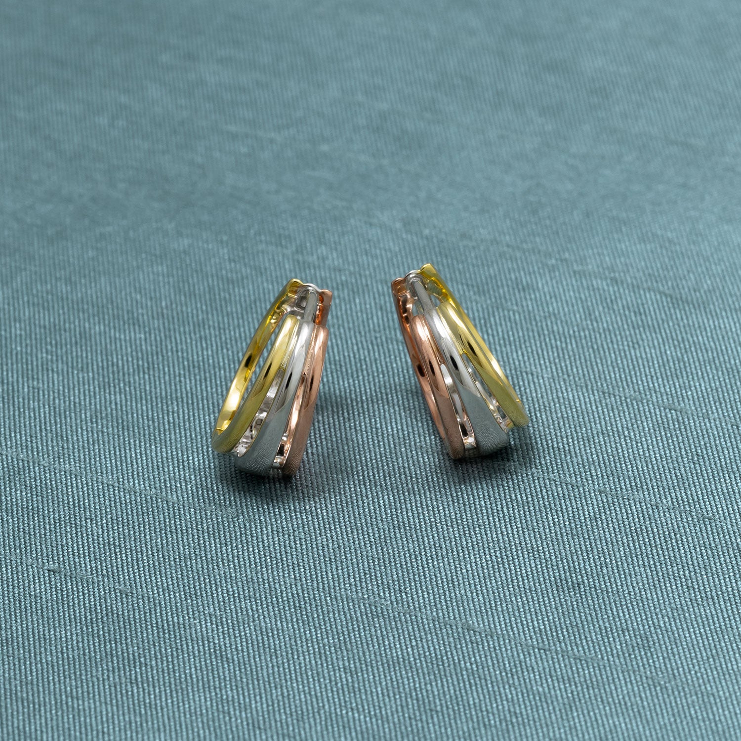 Hinged hoop earrings featuring three interwoven bands in sterling silver, rose gold, and gold tones, showcasing a polished, sculptural design in fine silver jewellery.