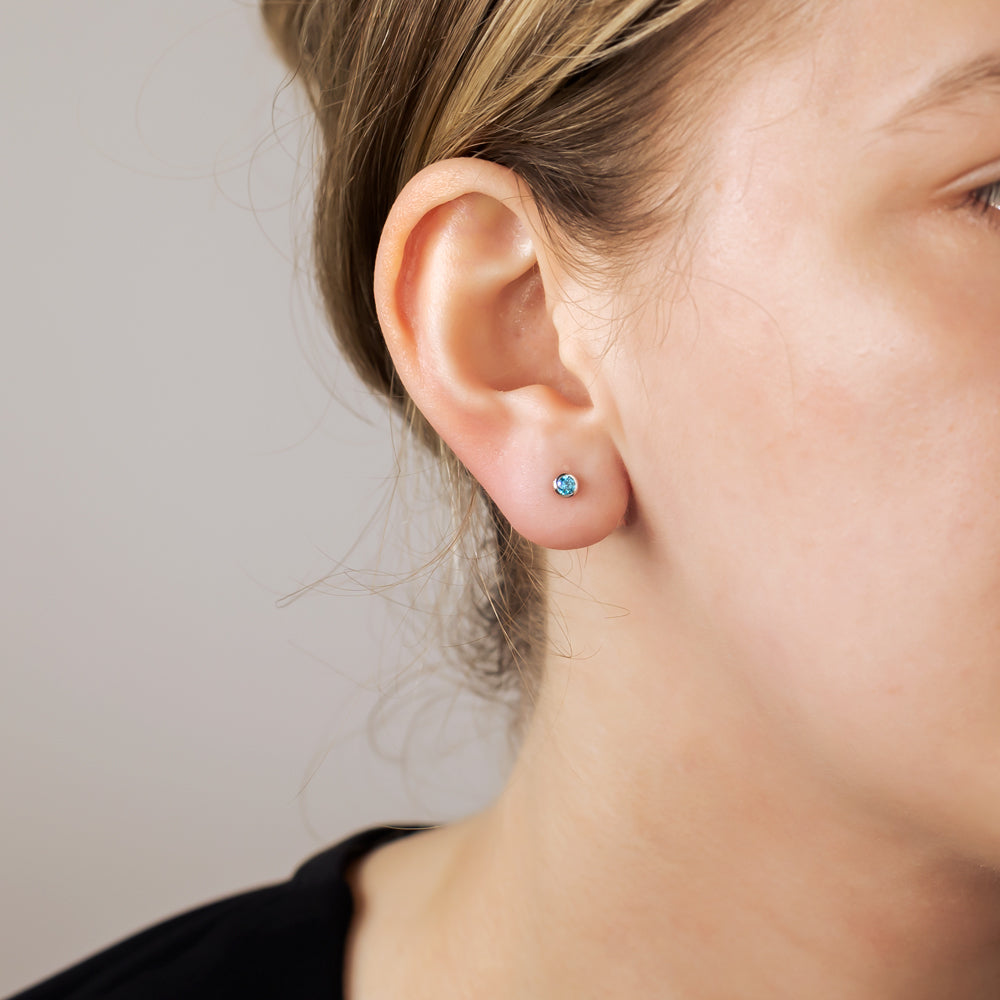 Sterling silver stud earrings featuring 3mm brilliant cut aqua stones, displayed on an ear, highlighting a subtle and refined silhouette in contemporary silver jewellery design.
