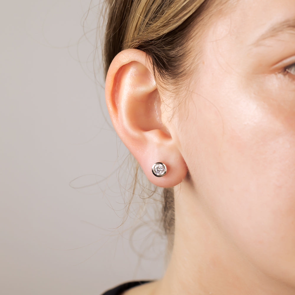 Close-up of a single stud earring featuring a brilliant-cut clear stone set in sterling silver, worn on the earlobe against a neutral background.
