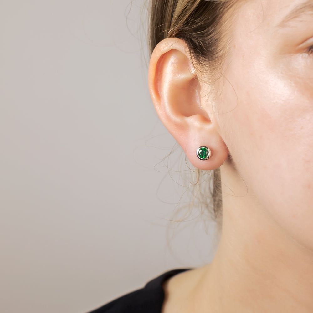 Close-up of a single sterling silver stud earring set with a brilliant-cut 5mm green stone, worn on a model's ear against a neutral background.