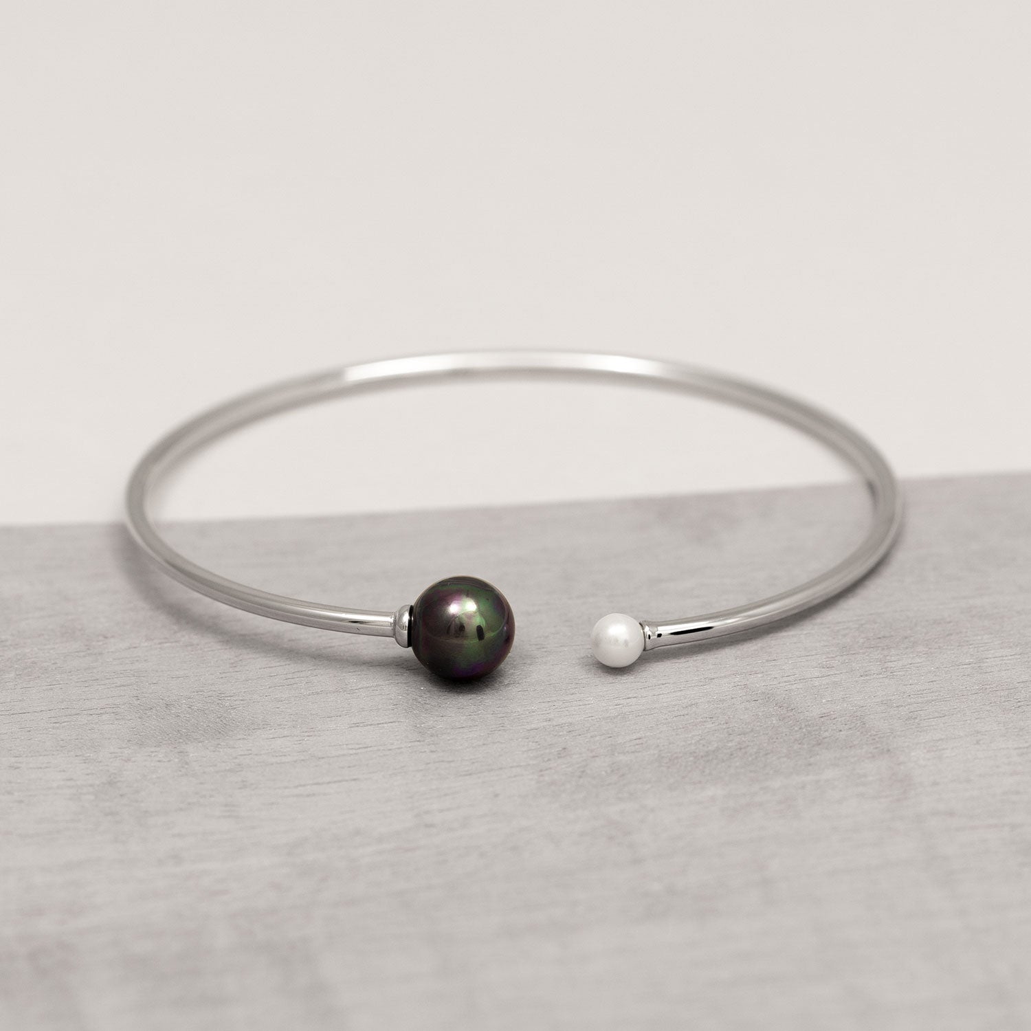 Sterling silver flexi cuff bracelet featuring contrasting black and white shell pearls at each open end, showcasing a minimalist and sculptural design.
