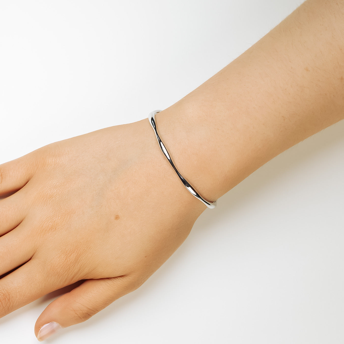 Slim sterling silver cuff bangle with a graceful wave-inspired curve, offering a minimalist and sculptural look in contemporary British silver jewellery.