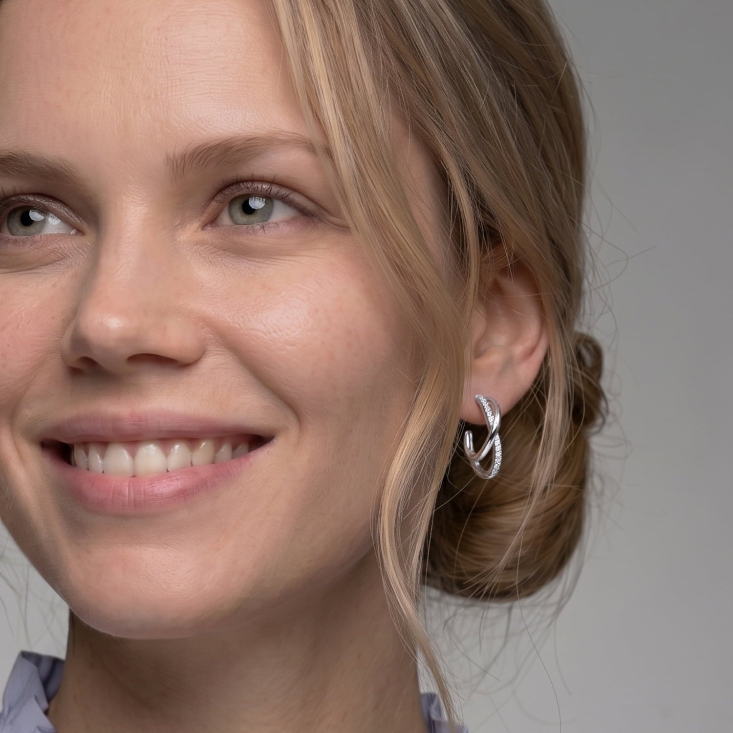 Model wears medium sterling silver hoop earrings featuring an elegant crossover wave design accented with pavé-set stones