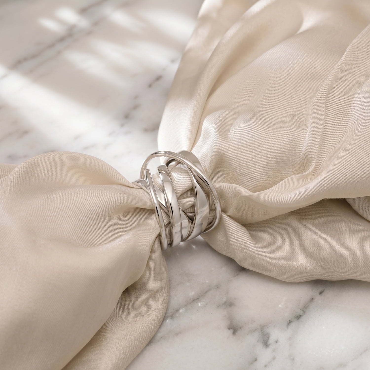 A multistranded polished sterling silver ring displayed on cream fabric on a marble background.