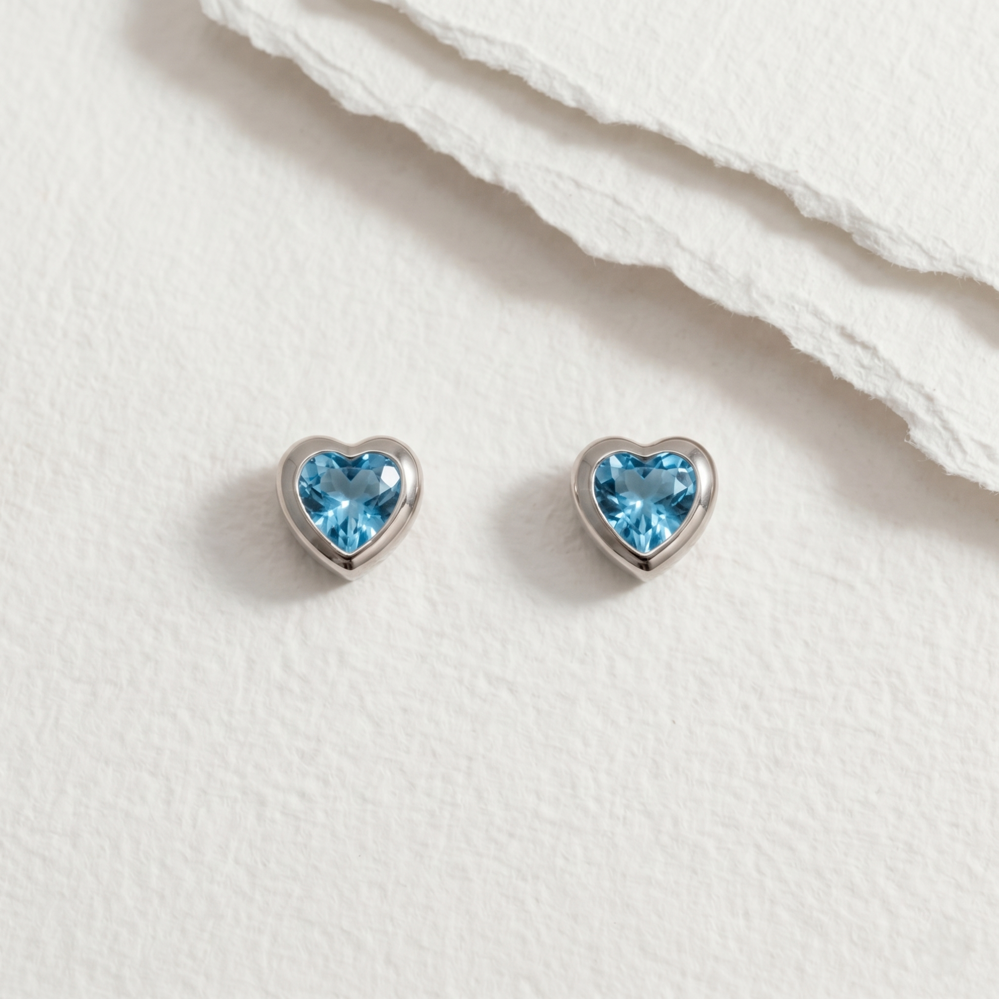 Heart-shaped blue topaz gemstone earrings on a paper background