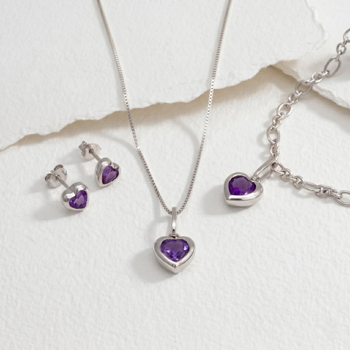 Silver jewellery set with purple amethyst heart-shaped stones on a paper background