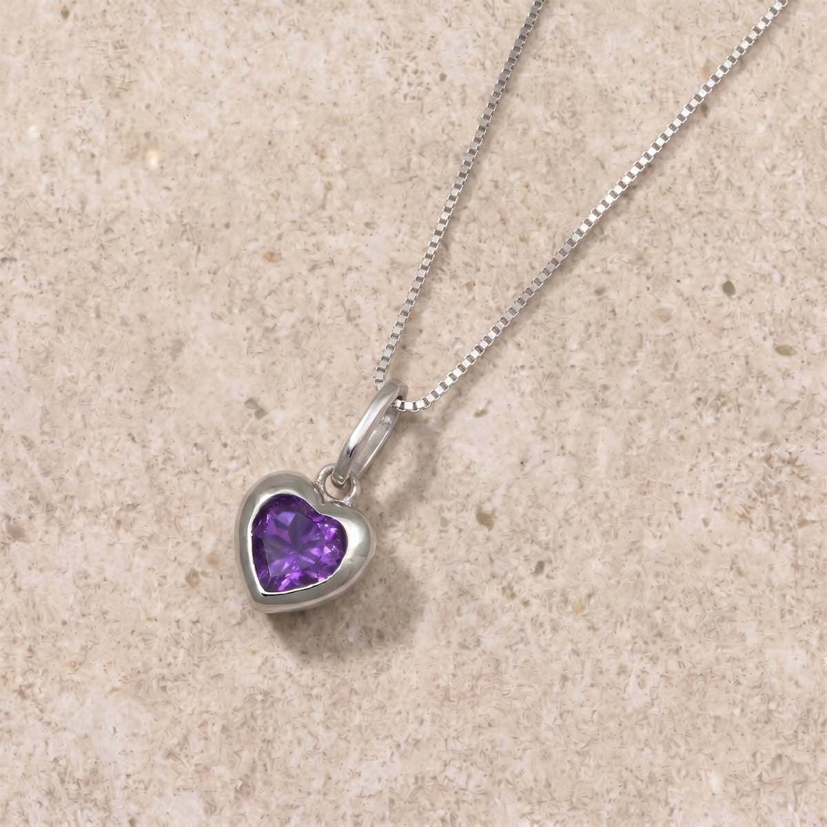 Silver necklace with a heart-shaped amethyst gemstone pendant on a beige limestone background