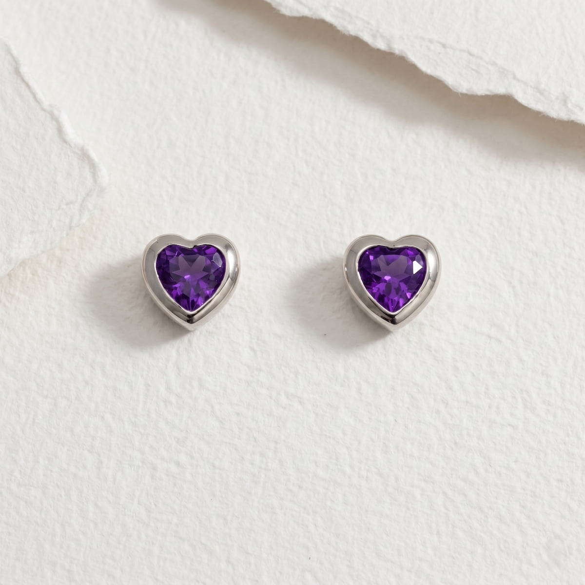 Heart-shaped amethyst gemstone silver earrings on a paper background
