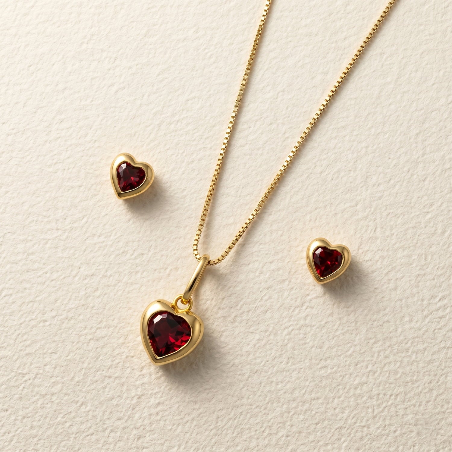 Yellow gold vermeil heart shaped garnet pendant and earrings on a cream background