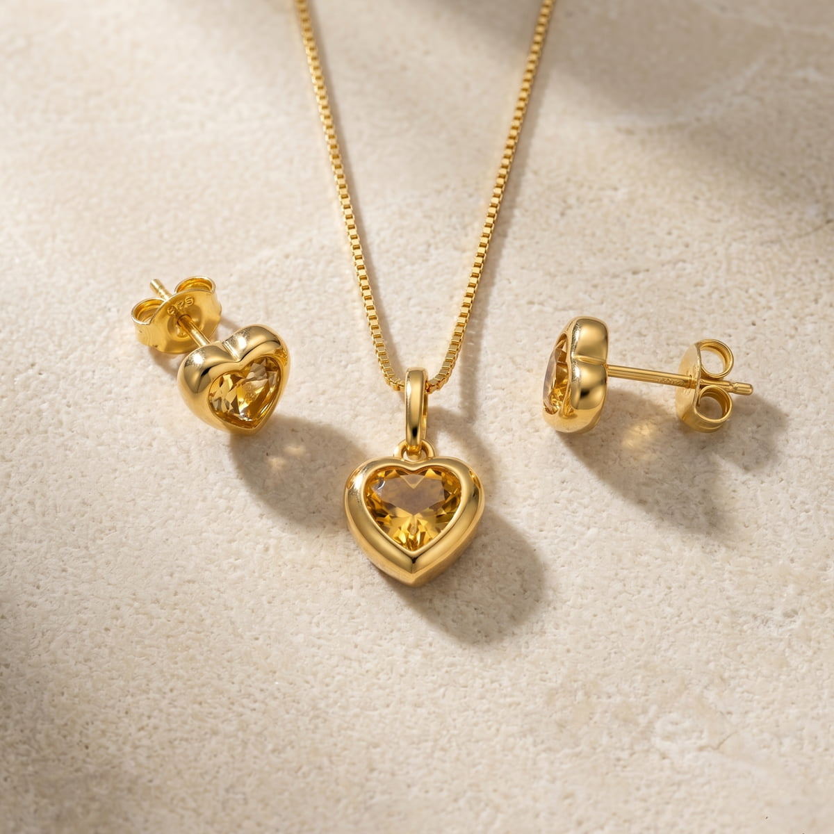 Gold vermeil heart-shaped pendant and earrings with citrene gemstones on a beige background