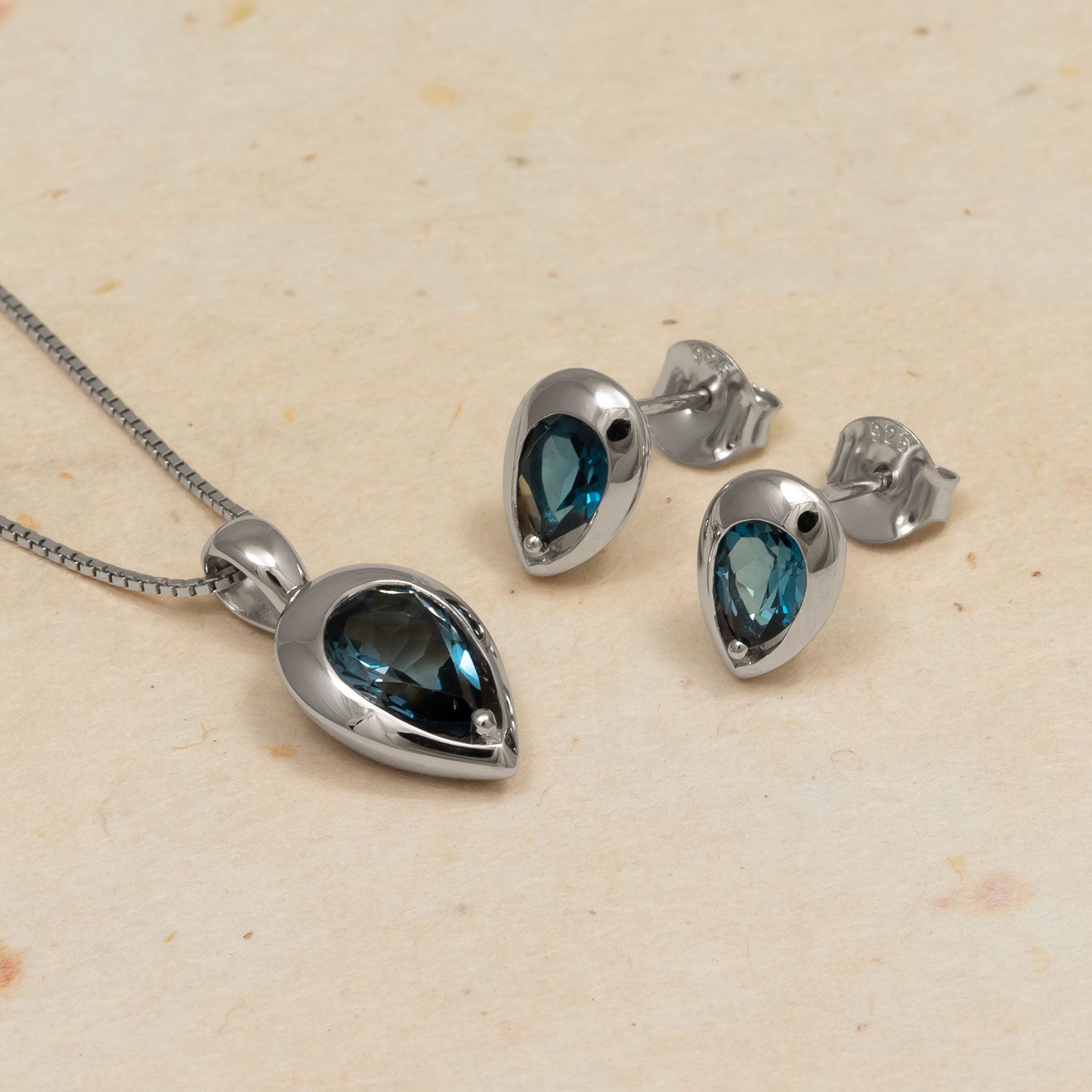 Sterling silver pendant and matching stud earrings set with deep blue London blue topaz teardrop gemstones, showcasing a sleek and sculptural modern design.