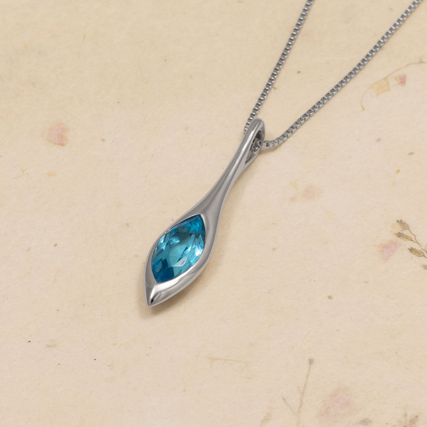 Teardrop-shaped pendant with blue gemstone on a beige background