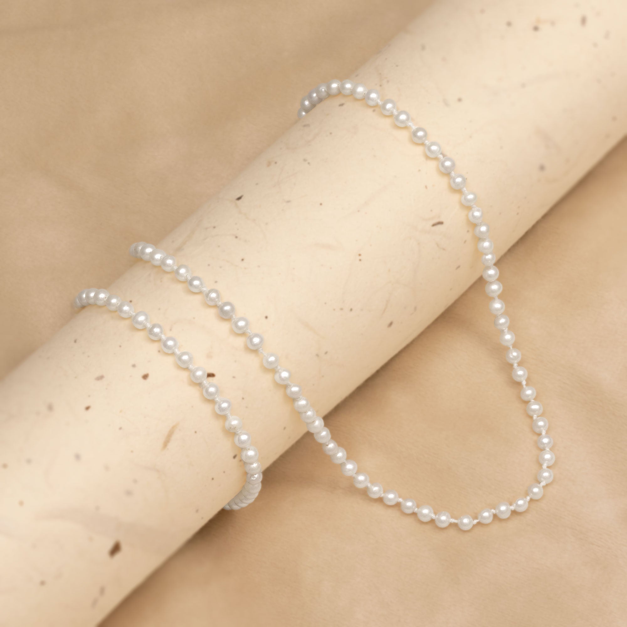 Pearl necklace and bracelet against a beige background