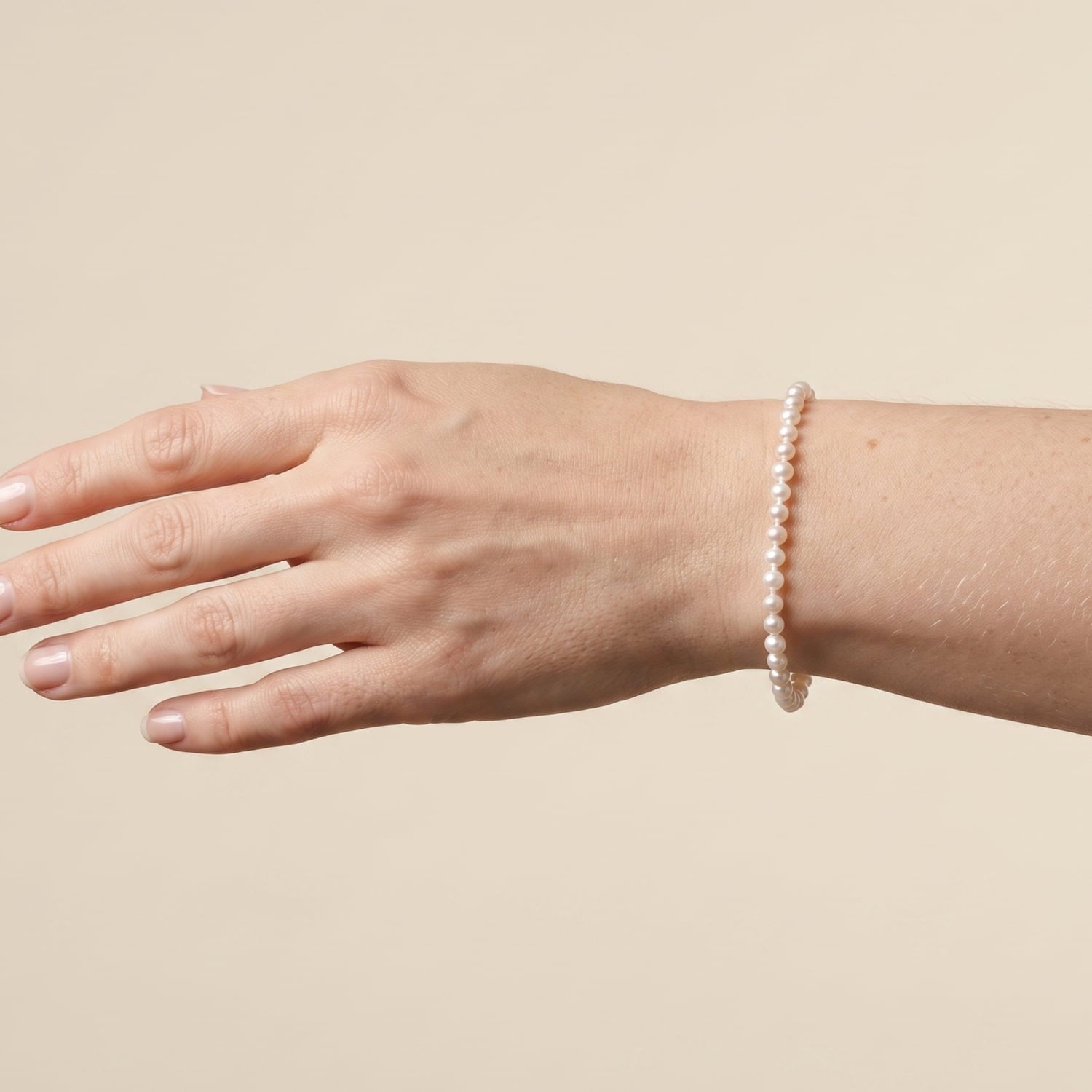 Model wears a bracelet made of small, round, freshwater pearls with a silver lobster clasp and extension chain, shown on a plain white background.