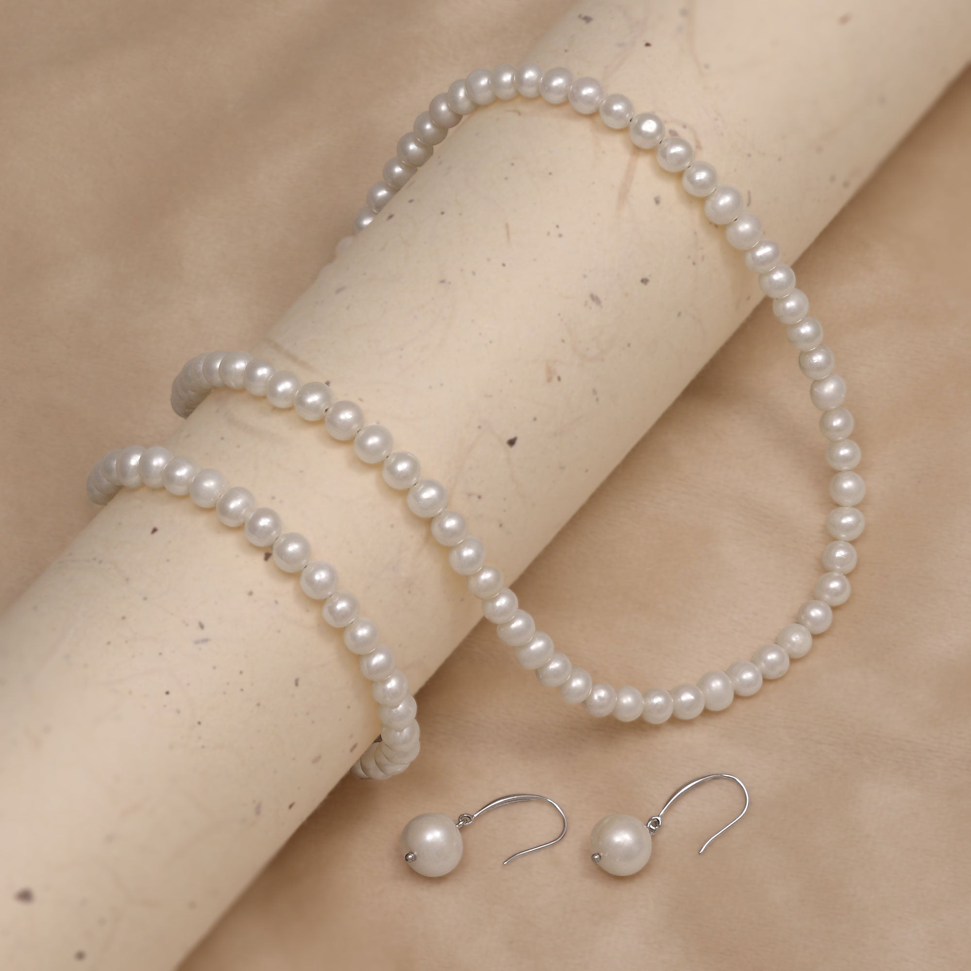 Pearl necklace, bracelet and earrings on a beige surface