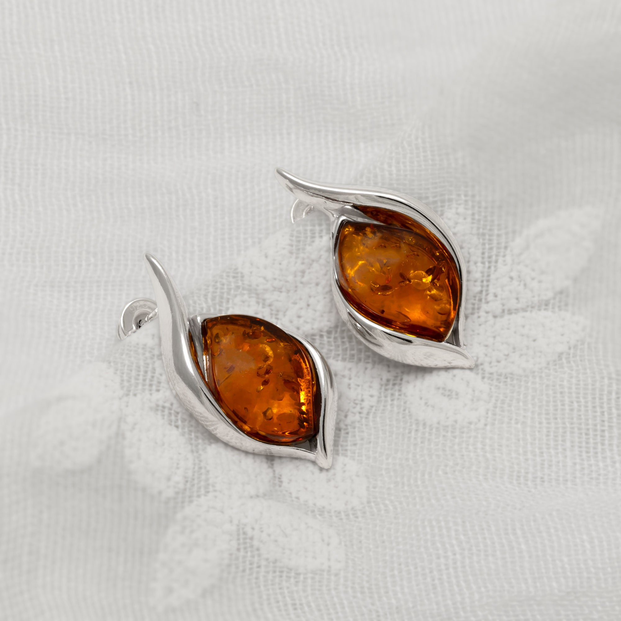 Pair of silver earrings with amber stones on a white fabric background