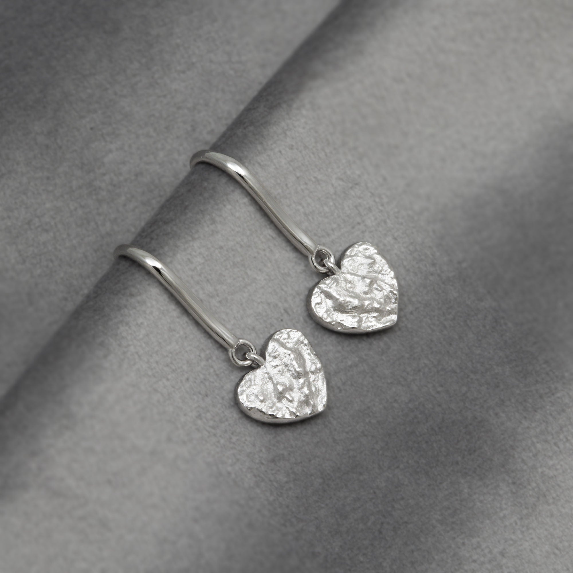 Pair of textured sterling silver heart-shaped earrings on a grey background