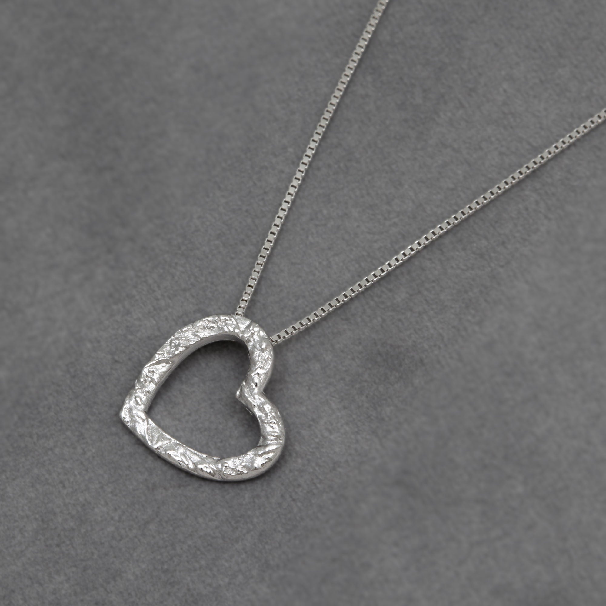Silver textured heart-shaped pendant necklace on a grey background
