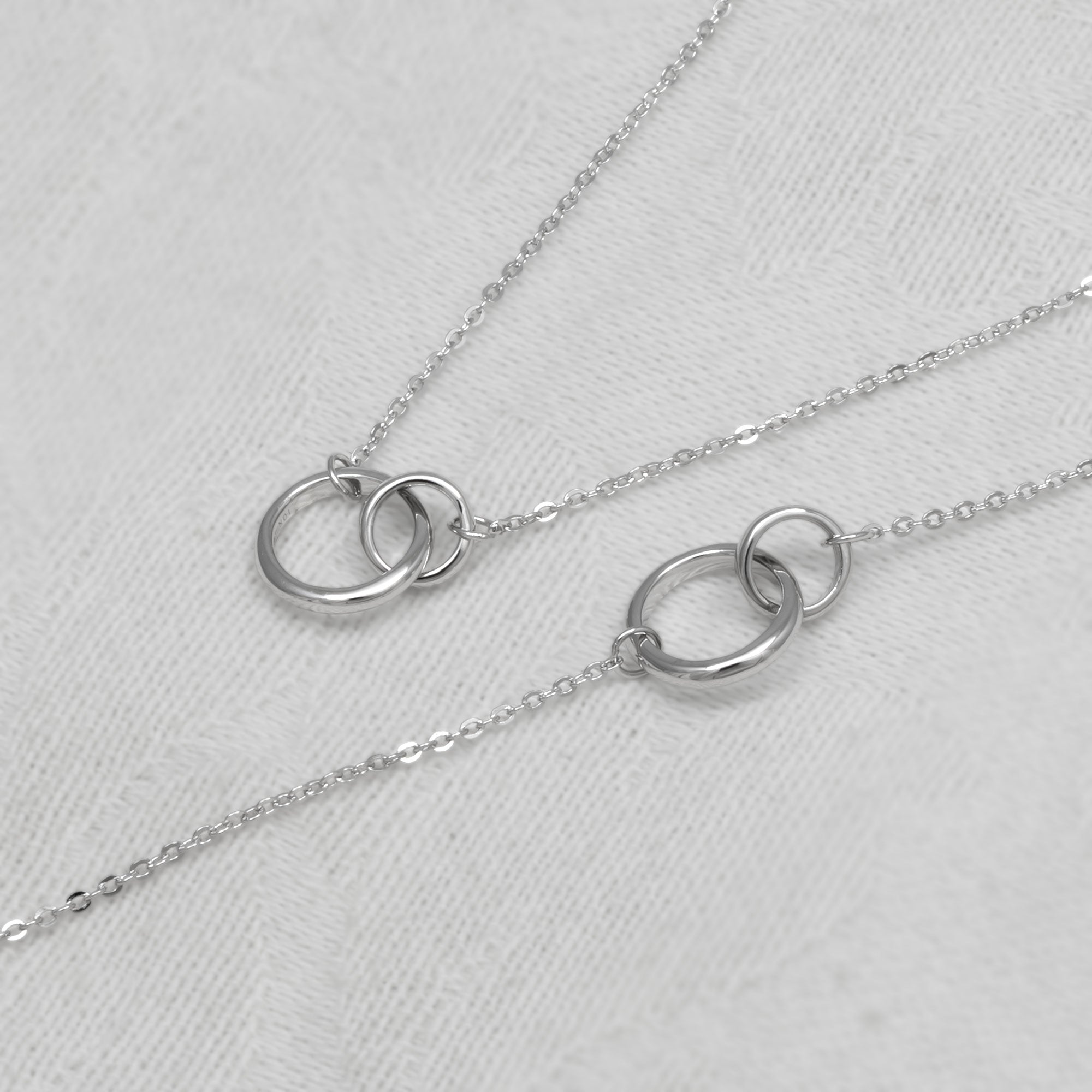 Silver necklace and bracelet with interlocking rings on a white background