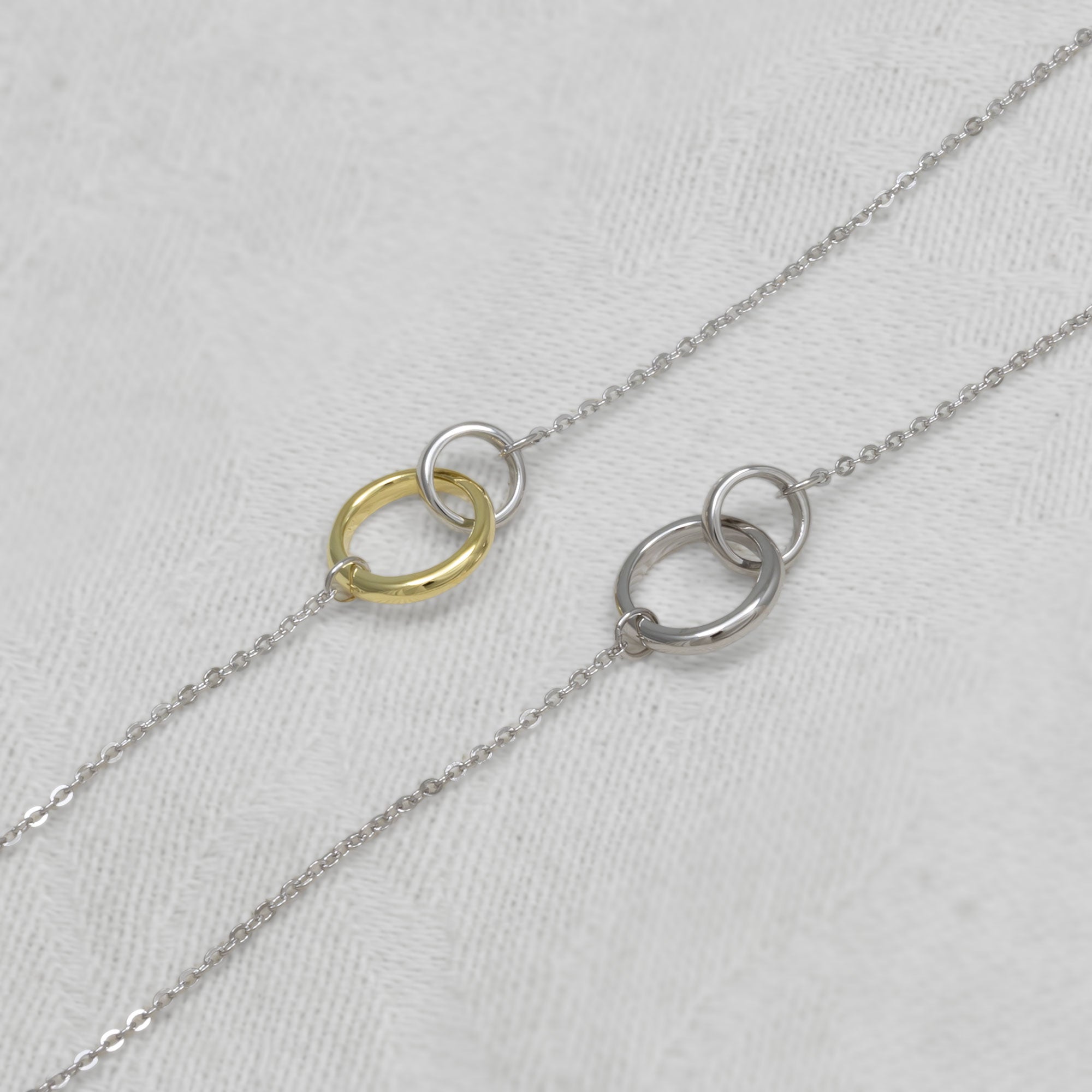 Two interlocking circle bracelets in gold vermeil and silver on a light gray background