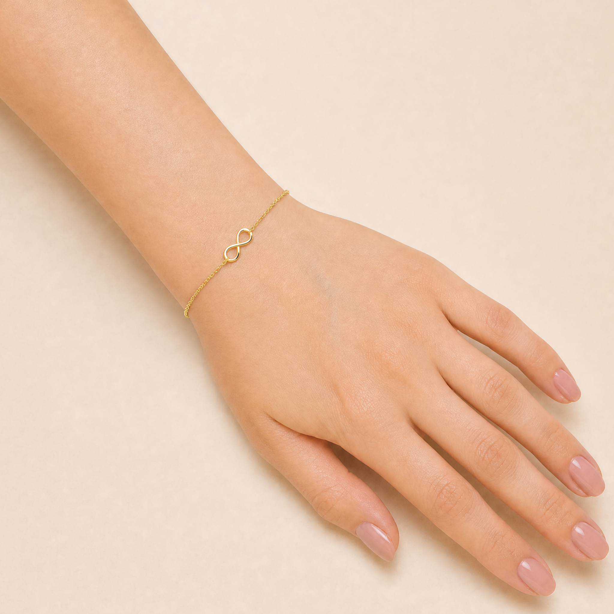 A delicate gold vermeil infinity bracelet worn on a person's wrist, shown against a soft beige background.