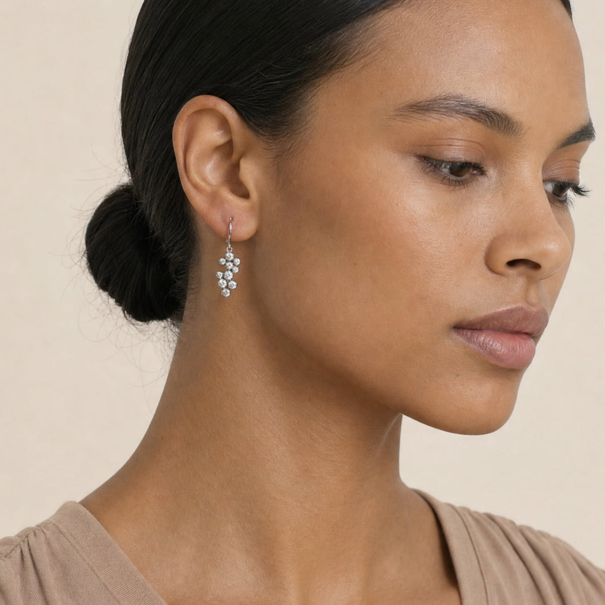 A close-up of a woman wearing a silver-toned drop earring with small clear stones, shown against a plain beige background.