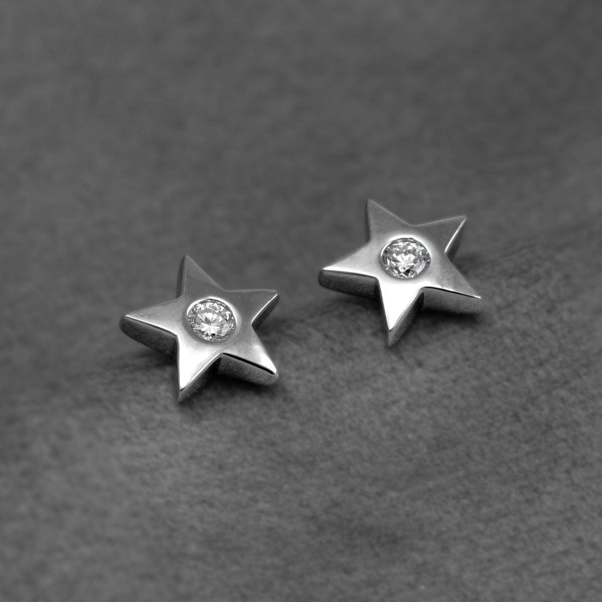 A pair of silver star-shaped stud earrings, each featuring a round lab grown diamond in the center, set against a plain grey background.