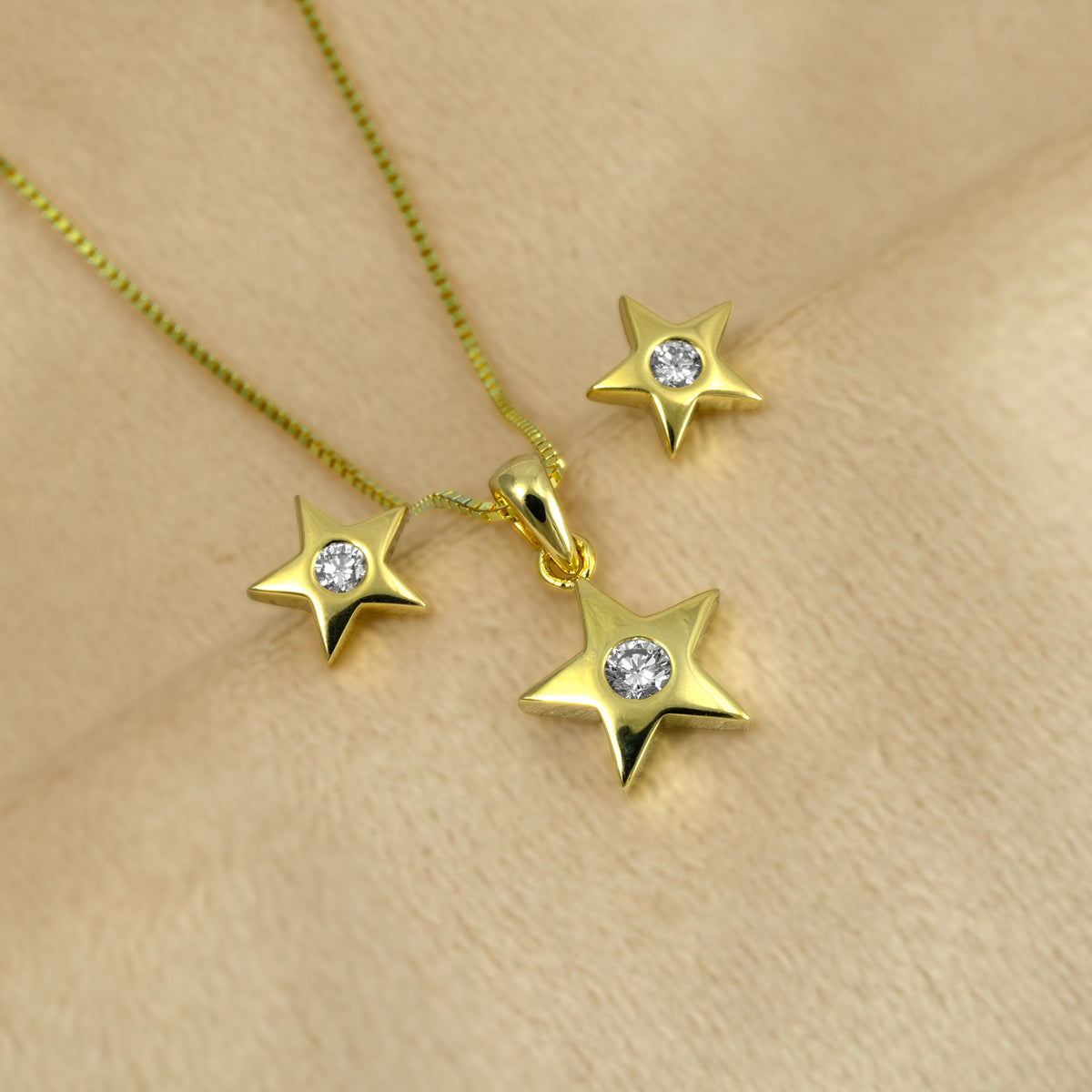 Gold vermeil star pendant with matching star-shaped stud earrings, each featuring a clear lab grown diamond, displayed on a soft beige textured background.