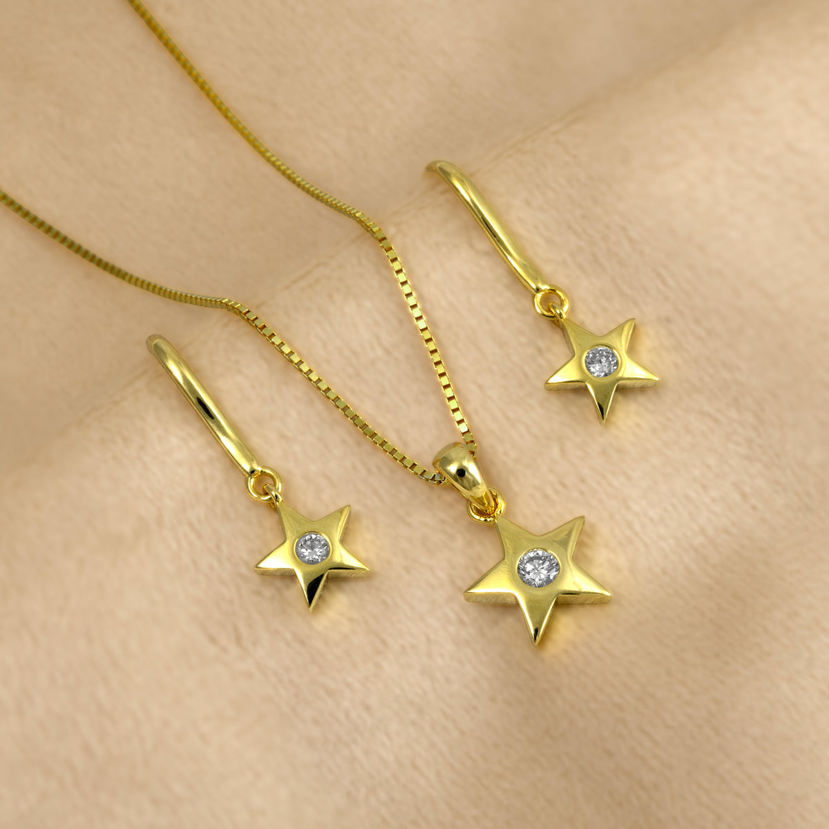 Gold vermeil star pendant necklace and matching drop earrings with lab grown diamonds, arranged on a soft beige fabric background.