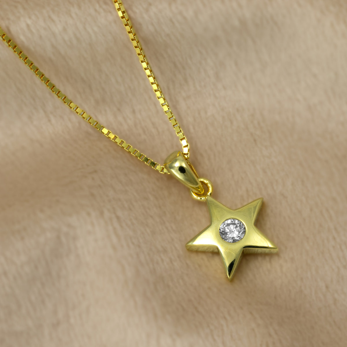 A gold vermeil star pendant with a lab grown diamond in the center, suspended from a gold vermeil box chain against a plain beige background.