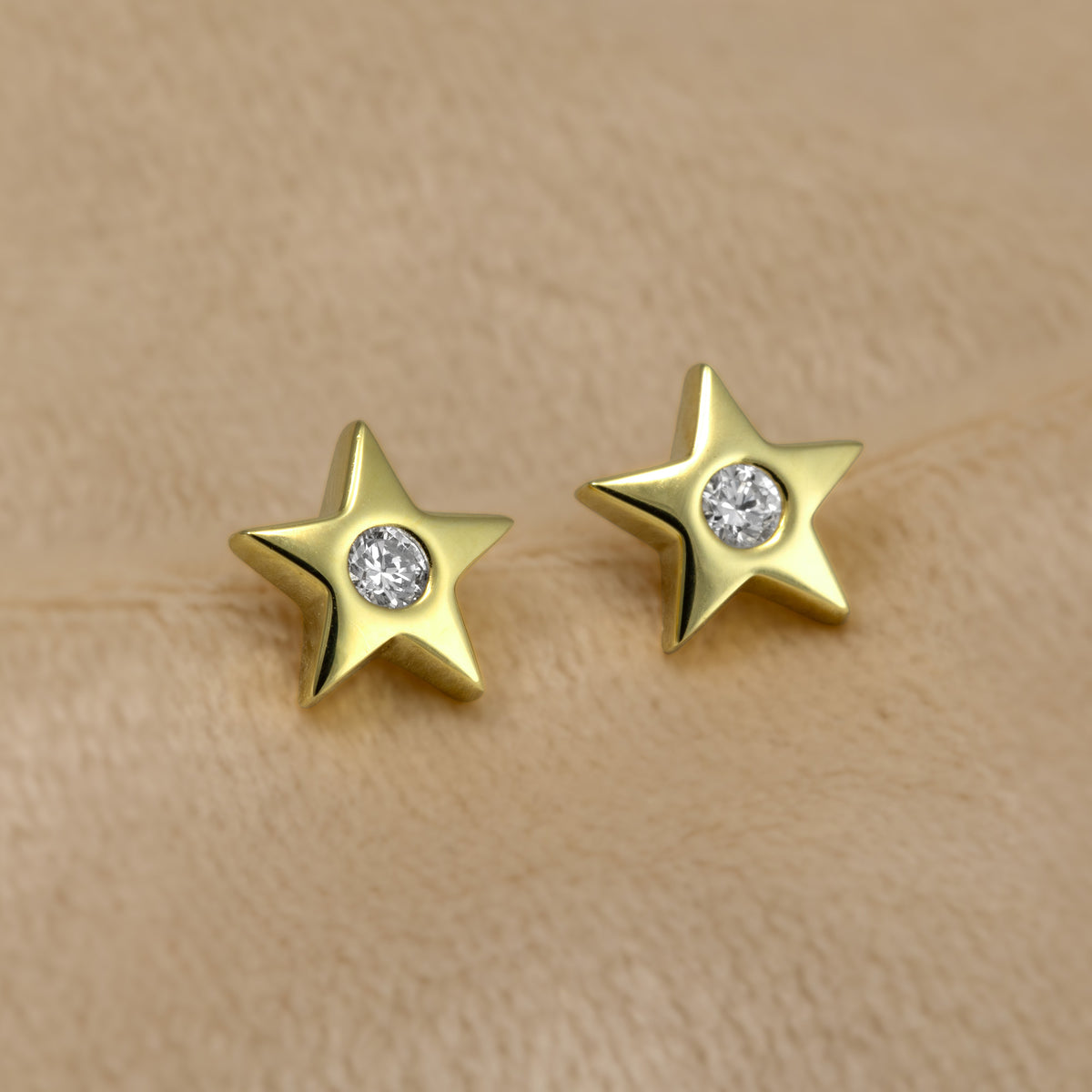 A pair of gold vermeil star-shaped stud earrings, each featuring a round lab grown diamond in the center, set against a cream fabric background.