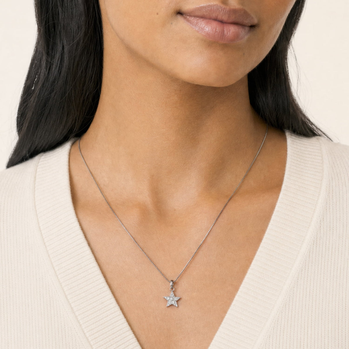 A close-up of a woman wearing a silver star pendant necklace fully set with pavé lab grown diamonds, styled with a cream ribbed V-neck top.