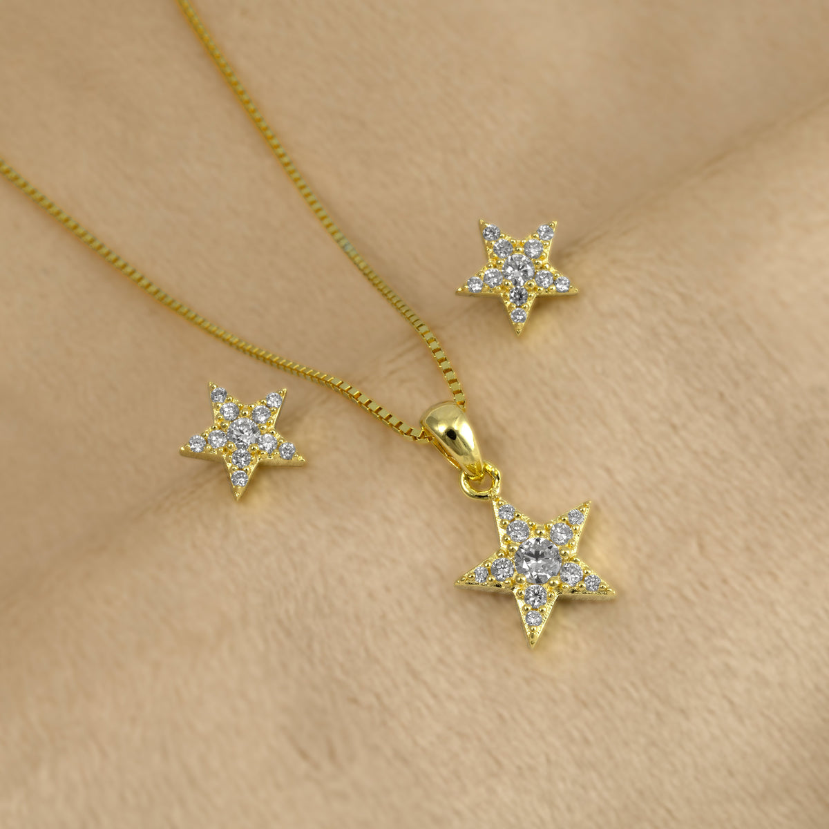 Gold star-shaped pendant and matching stud earrings set with lab grown diamonds, displayed on a soft beige surface.