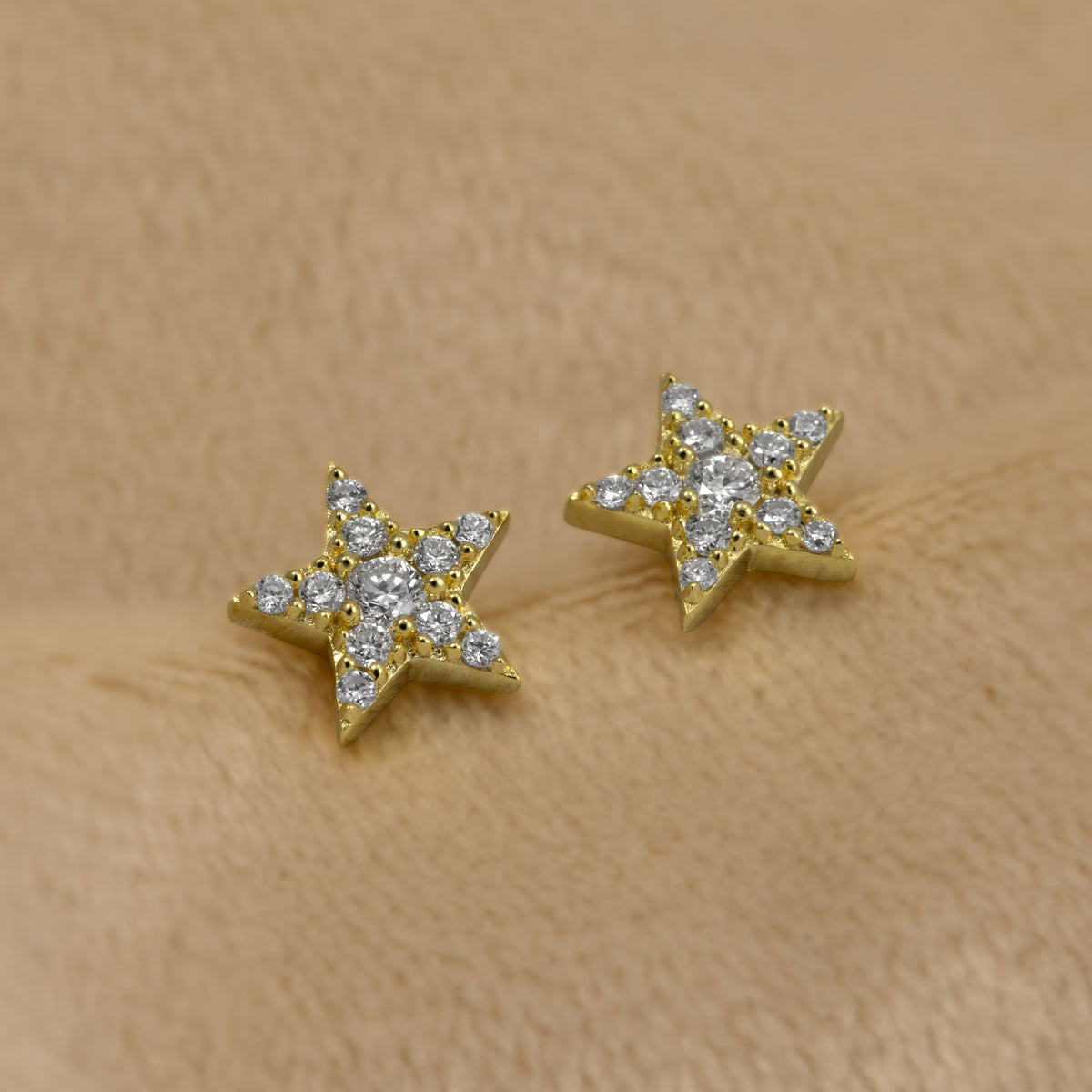 A pair of gold vermeil star-shaped stud earrings fully set with pavé lab grown diamonds, shown on a cream background.