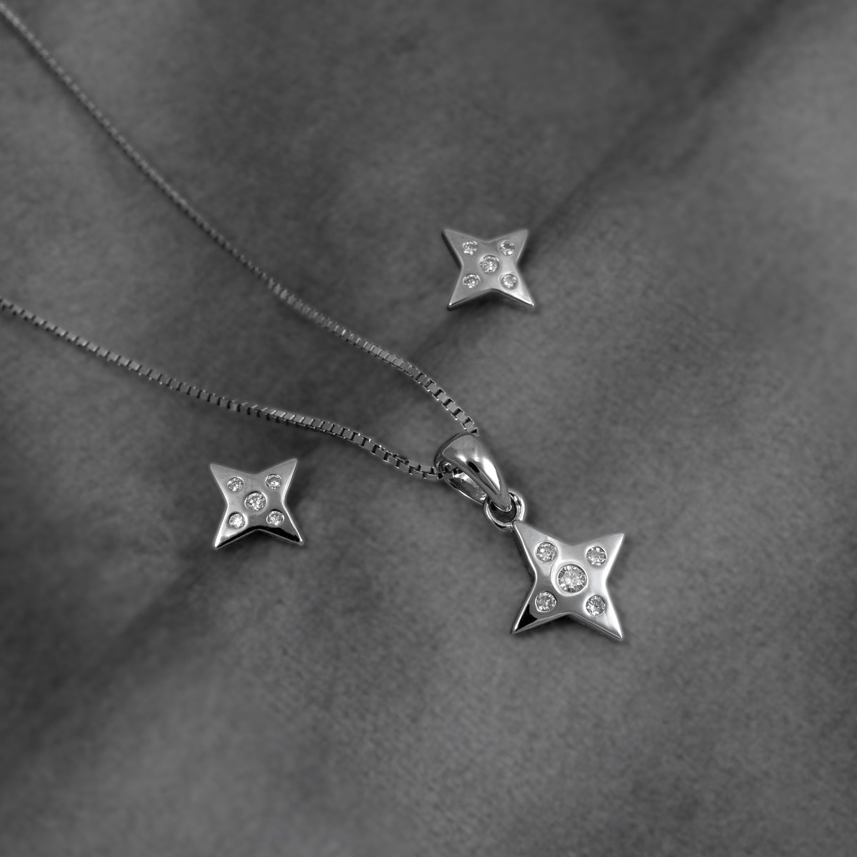 Silver jewellery set featuring a star pendant and matching star stud earrings,set with lab grown diamonds, displayed on a textured gray fabric background.