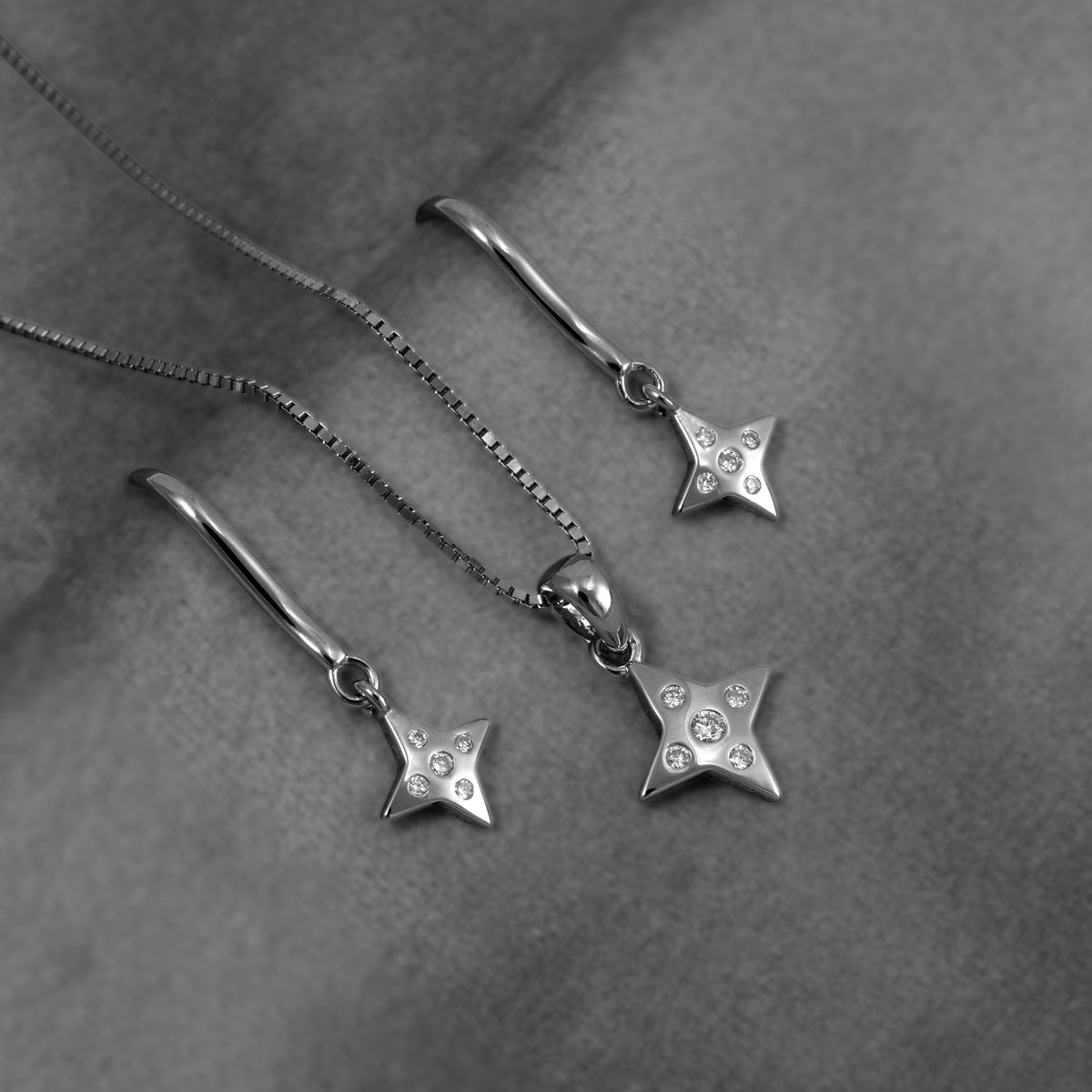 Sterling silver pendant and silver drop earrings featuring four-pointed star charms with lab grown diamonds, suspended from curved hook ear wires, shown on a grey background.