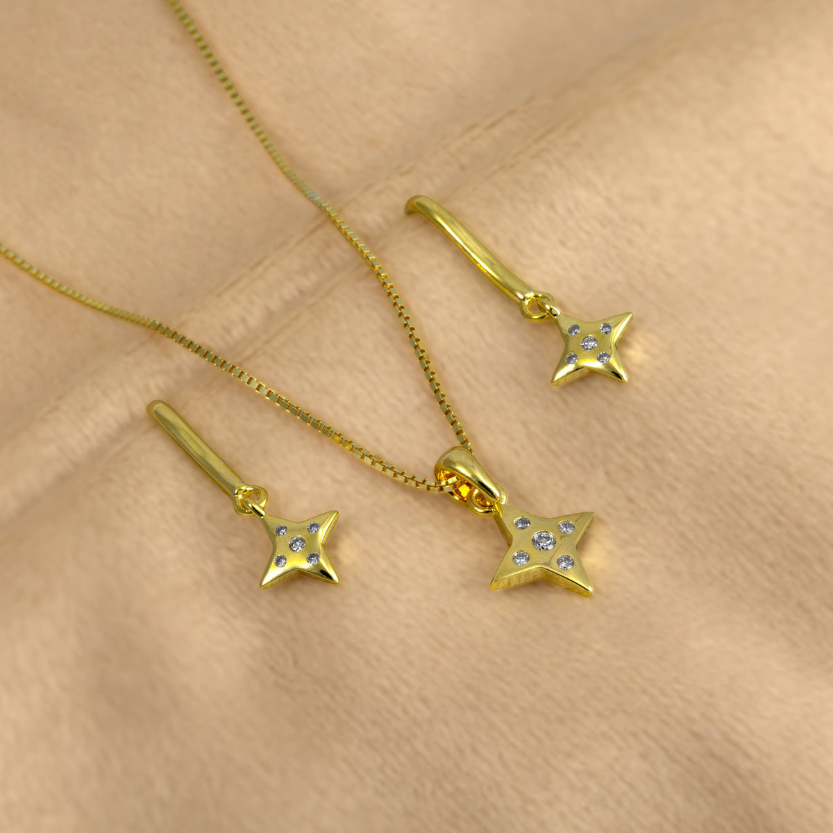 A gold vermeil jewellery set of drop earrings and matching pendant with four-pointed star charms, each adorned with five lab grown diamond stones.