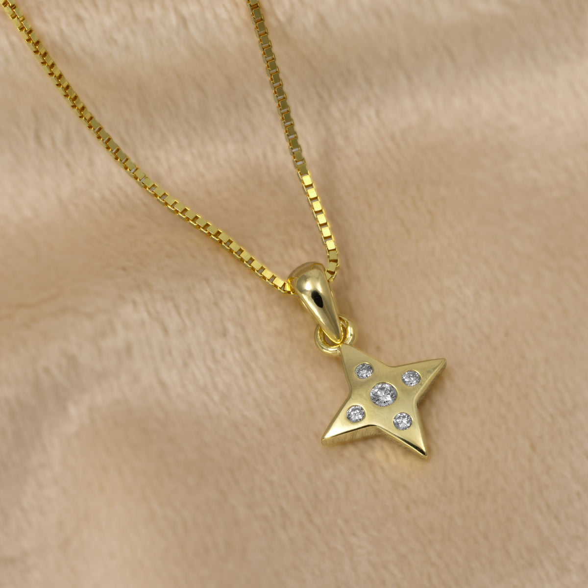 A gold vermeil star-shaped pendant necklace with five lab grown diamonds, suspended from a gold box chain against a cream background.