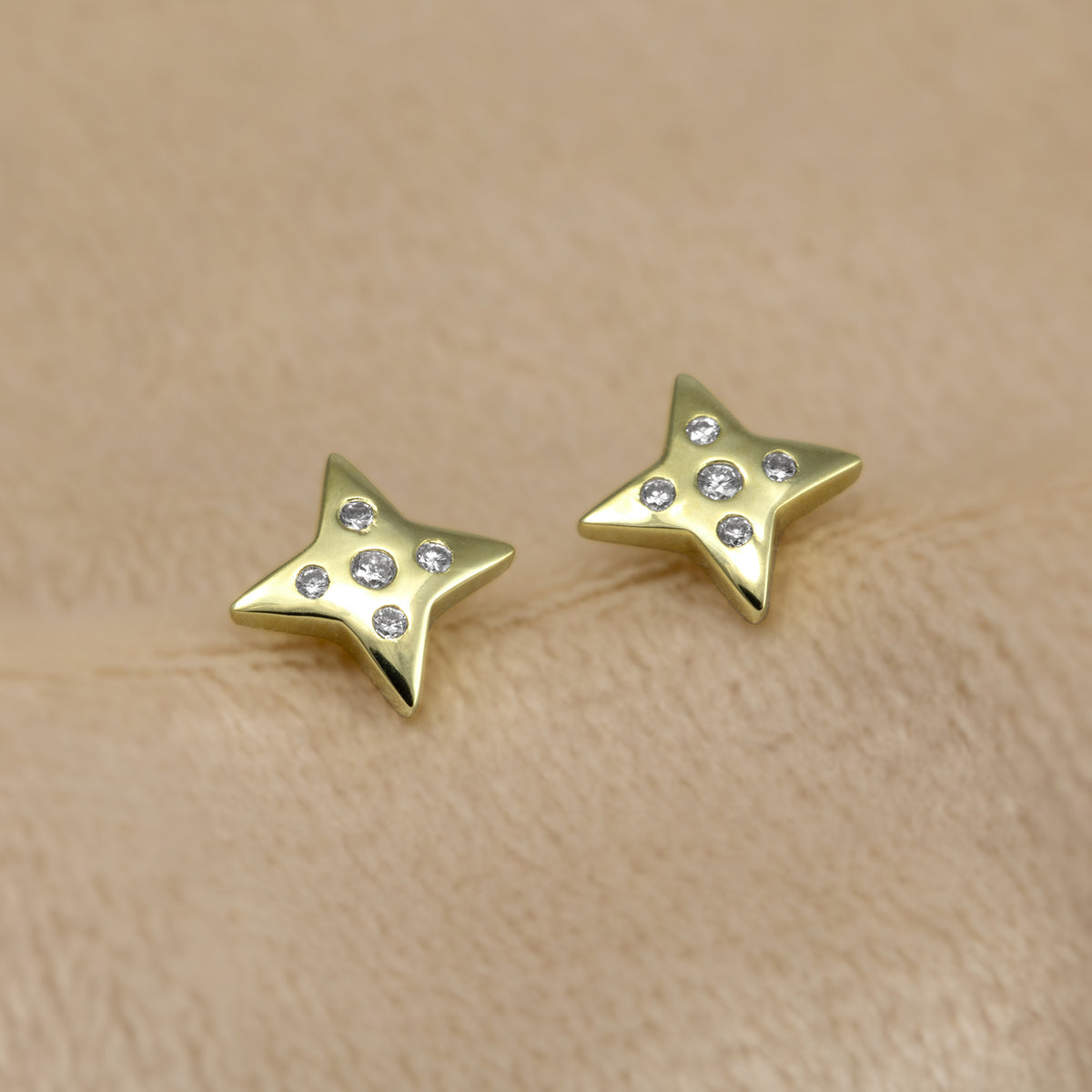 A pair of gold vermeil star-shaped stud earrings, each adorned with five clear lab grown diamonds, set against a cream background.