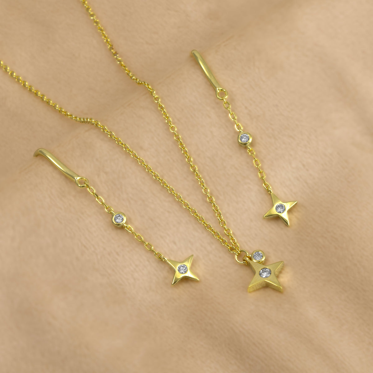 Gold vermeil jewellery set featuring a delicate chain necklace and matching drop earrings with star-shaped pendants, each accented with lab grown diamonds, displayed on a soft beige fabric background.