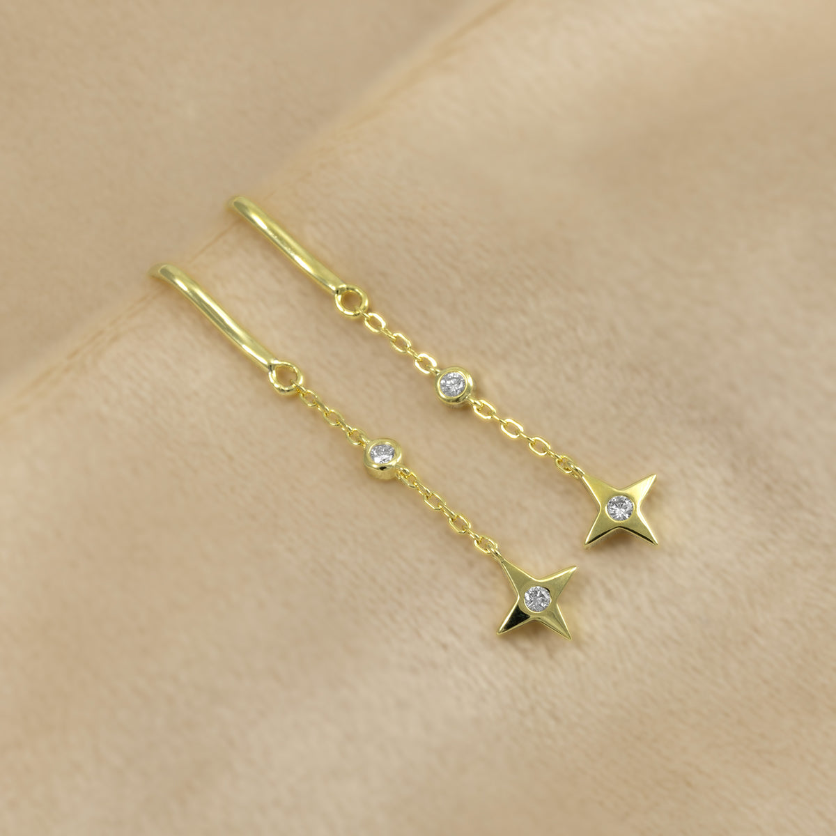 A pair of gold vermeil drop earrings with a hook back, round bezel-set lab diamonds, and a dangling star-shaped charm set with another lab diamond, shown on a cream background.